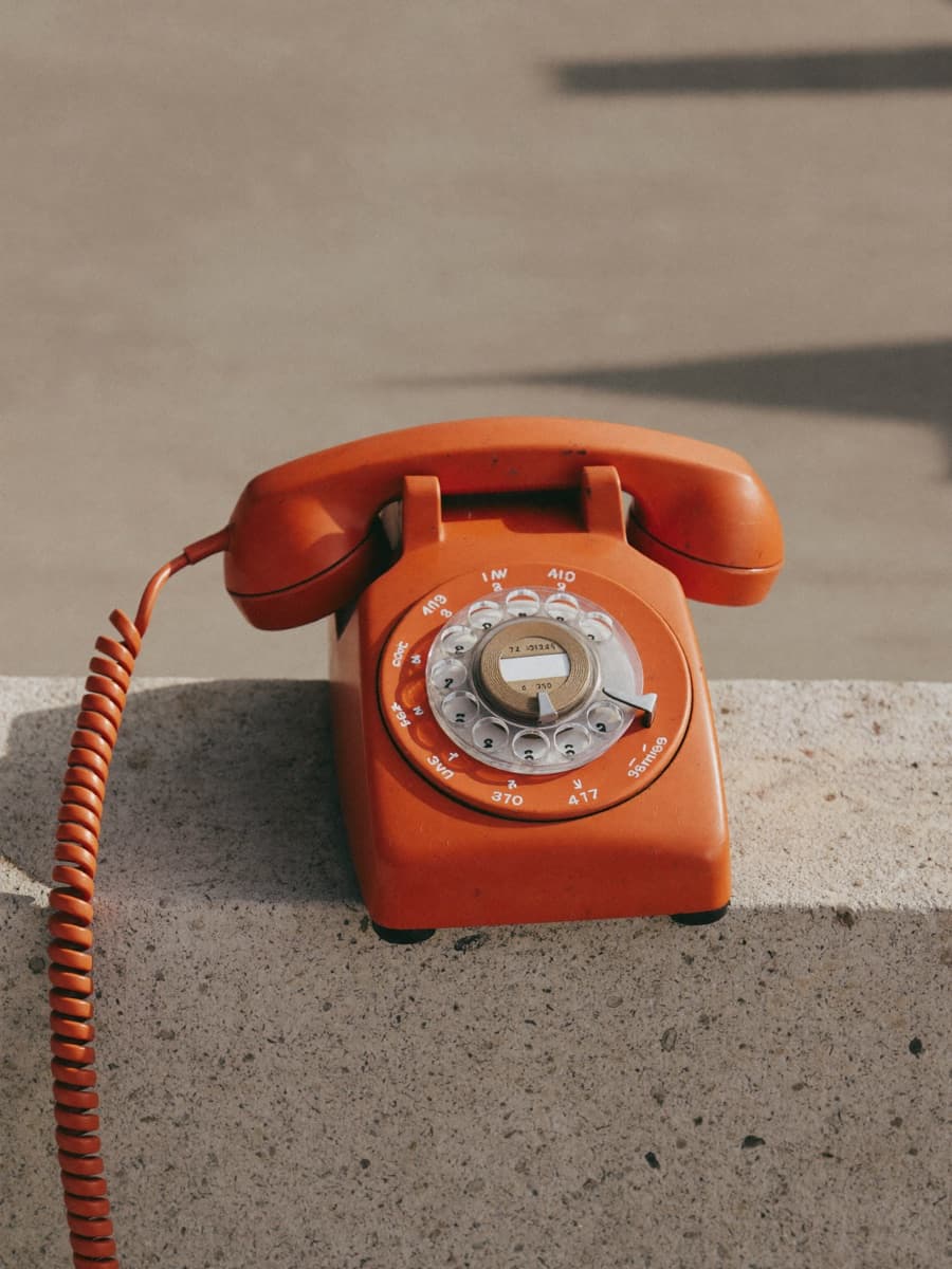 A safety-orange rotary telephone on a concrete ledge